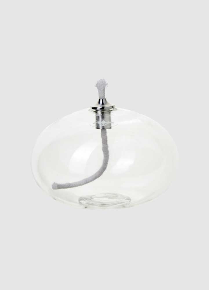 Oljelampa med ofärgat klarglas ovalformad med en bomullsveke som sticker upp ur en silverfärgad kon, lampan är placerad mot en vit bakgrund.
