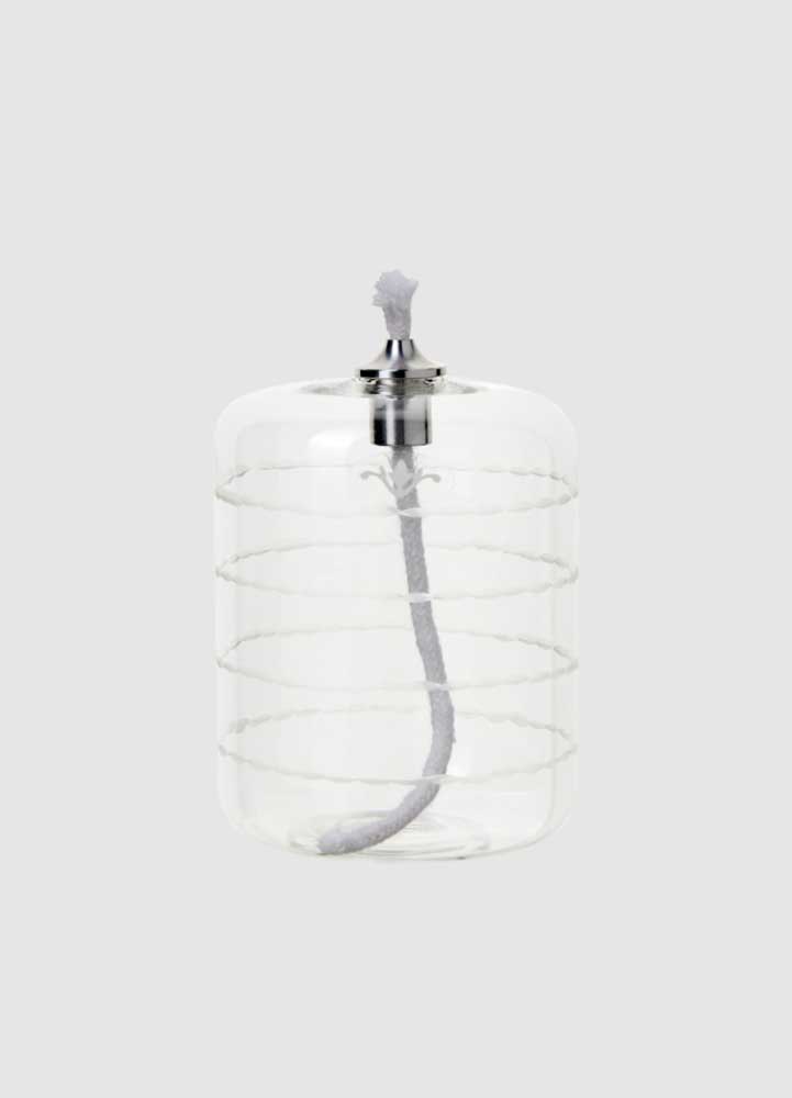 Oljelampa med ofärgat klarglas med vågrandigt mönster, mellanhög cylinderformad med en bomullsveke som sticker upp ur en silverfärgad kon.
